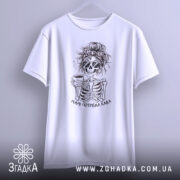 Футболка мамі потрібна кава, біла, підвішена на вішалці, фон світло-сірий, принт з черепом у сонцезахисних окулярах, що тримає чашку кави, з написом 'Мамі потрібна кава'.