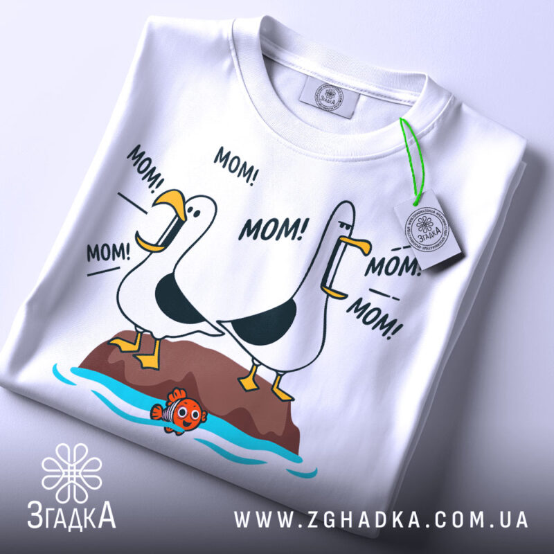 Футболка мамин день, біла, зображена з верхнього ракурсу, на фоні світло-сірого кольору, принт з двома птахами, що кричать 'MOM!', з зеленим ярликом.