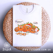 Футболка мандариновий маніяк, біла, складена на плетеному кошику, з принтом мандаринів, що спілкуються, на фоні натурального матеріалу.