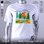 Футболка мандруй гори, біла, зображена на манекені, фон світло-сірий, принт з горами, деревами та річкою в яскравих кольорах.