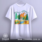 Футболка мандруй гори, біла, підвішена на вішалці, фон світло-сірий, принт з горами, деревами та річкою, вигляд спереду.