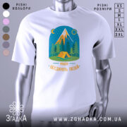 Футболка мандри обʼєднують білого кольору, зображена на манекені з блискучою поверхнею, фон нейтральний сірий. Принт містить малюнок гір, лісу та намету, виконаний у яскравих кольорах з текстом 'Мандри обʼєднують людей'.