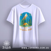 Футболка мандри обʼєднують білого кольору, підвішена на вішалці, фон світлий. Принт з малюнком гір, лісу та намету, кольори яскраві, текст 'Мандри обʼєднують людей' розташований внизу.