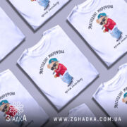 Футболка мастодонт мікрофона білого кольору, зображена з фронтального ракурсу на манекені, фон нейтральний, принт з ведмедиком у червоній куртці та синій кепці, що тримає мікрофон, текст під принтом: "кринж стендапу".