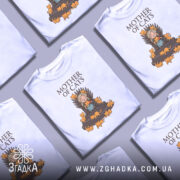 Футболка мати котів білого кольору, зображена з фронтального ракурсу на манекені, фон градієнтний сірий, принт з малюнком дівчини на троні з котами, напис 'MOTHER OF CATS' зверху.