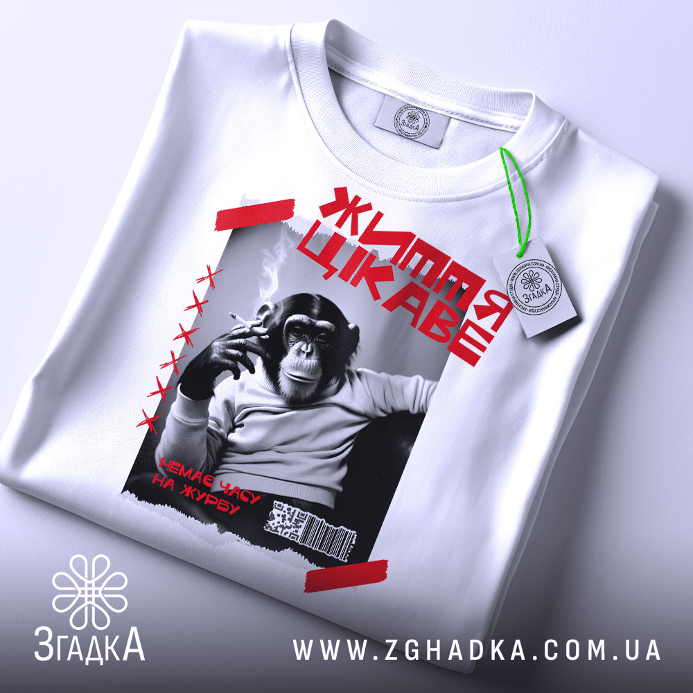 Футболка мавпа життя цікаве. Біла футболка, складена на столі, з принтом чорного мавпи, що курить. На фоні світло-сірого кольору, з зеленим ярликом.