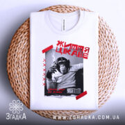 Футболка мавпа життя цікаве. Біла футболка, складена на плетеному кошику, з принтом чорного мавпи, що курить. На фоні світло-сірого кольору.