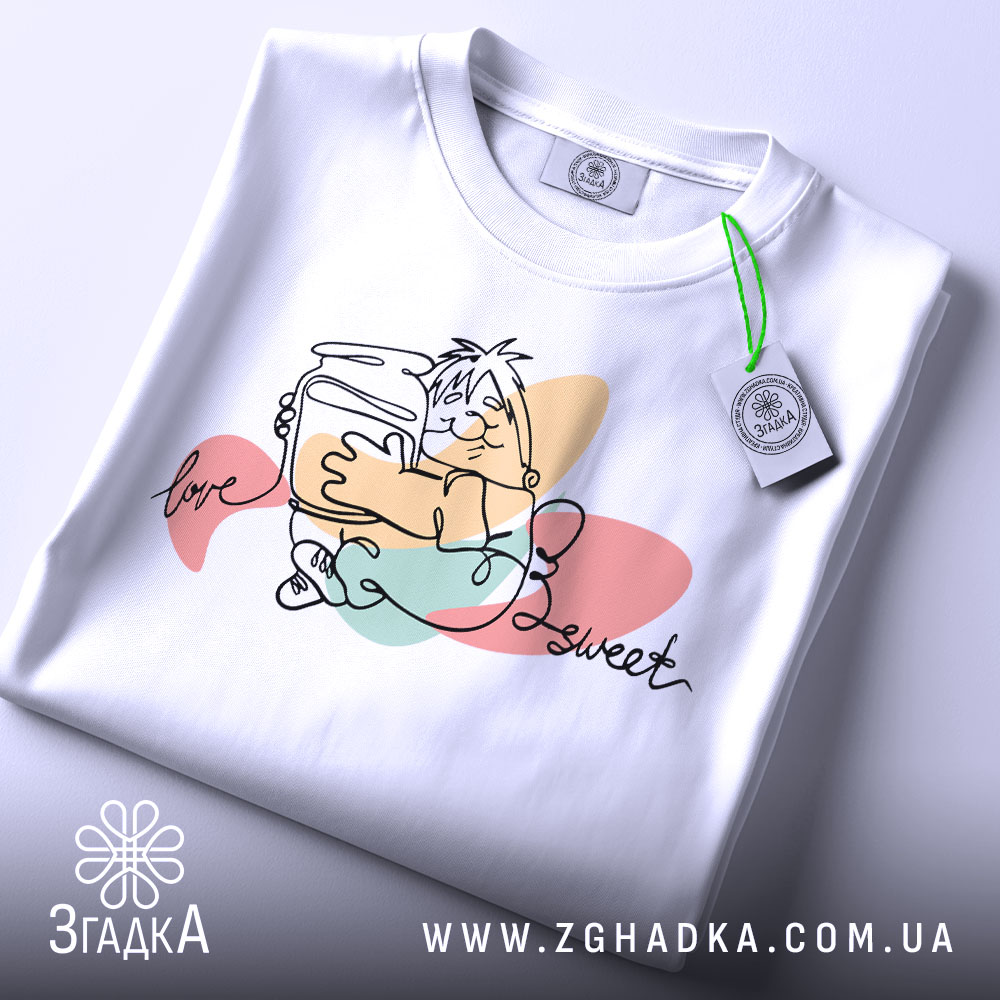 Футболка медовий настрій, біла, зображена зверху, на фоні світло-сірого кольору, принт з малюнком персонажа, що тримає банку з медом, з написом 'love sweet', на комірці видна етикетка.