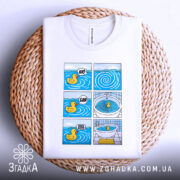 Футболка Мем Качечка, біла, лежить на плетеному кошику, фон світлий, принт з шести коміксів з качечкою, яскраві кольори, деталі принта чіткі.