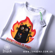 Футболка Мем Кіт білого кольору, зображена зверху, фон світло-сірий, принт з чорним котом у вогняному обрамленні, текст "EVERYTHING IS FINE!" під котом, на комірці видно етикетку.