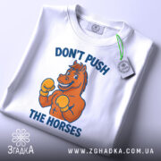Футболка мем Не жени коней, складена біла футболка з принтом, зображення коня в боксерських рукавичках, ракурс зверху, фон світлий, текст синього кольору, на футболці є етикетка.