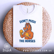 Футболка мем Не жени коней, складена біла футболка на плетеній основі, з принтом, зображення коня в боксерських рукавичках, ракурс зверху, фон світлий, текст синього кольору.