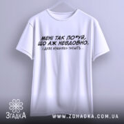 Футболка мені так по*уй, біла футболка, підвішена на вішалці, з чорним принтом, текст на грудях: 'МЕНІ ТАК ПО*УЙ, ЩО АЖ НЕВДОБНО. І ДАЖЕ НЕМНОЖКО ПОБЛЯТЬ...'. Фон світло-сірий.