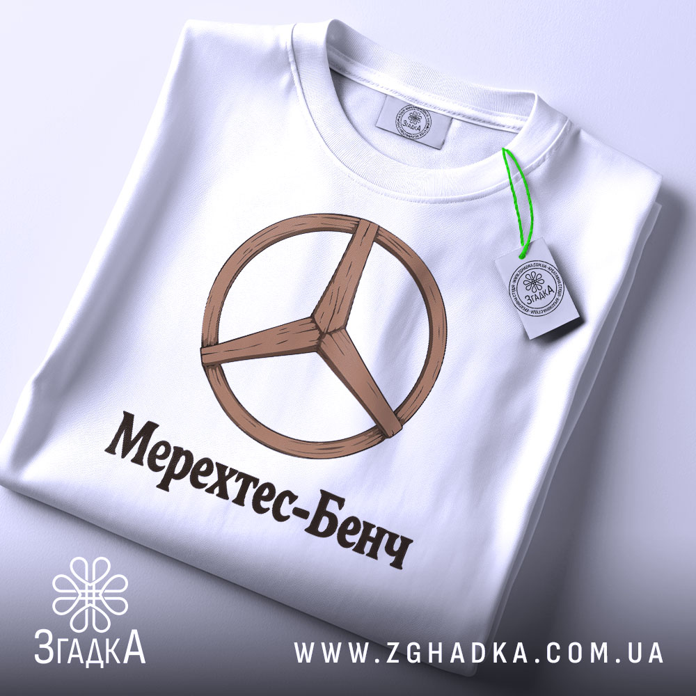 Футболка Мерехтес-Бенч стиль, біла, складена на столі, фон світло-сірий, принт з дерев'яним логотипом і написом 'Мерехтес-Бенч', на комірці видна етикетка.