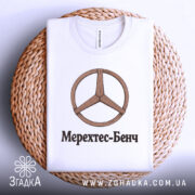 Футболка Мерехтес-Бенч стиль, біла, складена на плетеній кошику, фон світло-сірий, принт з дерев'яним логотипом і написом 'Мерехтес-Бенч'.