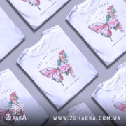 Футболка метелик квіти, біла, зображена на манекені, фон світло-сірий, принт з метеликом та квітами у пастельних тонах, текст "YOU ARE FREE to fly" та "SPREAD YOUR WINGS" під принтом.