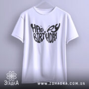 Футболка метелик вітання, біла, підвішена на вішалці, фон світло-сірий, принт чорного кольору з написом 'HAPPY BIRTHDAY' у формі метелика.