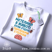 Футболка метелики в животі, білого кольору, складена на поверхні, фон світлий, принт з текстом та ілюстраціями метеликів і мозку, з етикеткою.