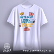 Футболка метелики в животі, білого кольору, підвішена на вішалці, фон світлий, принт з текстом та малюнками метеликів і мозку.