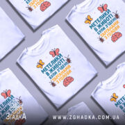 Футболка метелики в животі, білого кольору, складена на поверхні, фон світло-сірий, принт з текстом та малюнками метеликів і мозку, кілька футболок в кадрі.