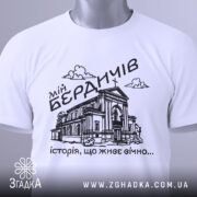 Футболка мій Бердичів, біла, зображена зверху, на плоскій поверхні, фон світло-сірий, принт чорного кольору з зображенням будівлі та написом 'історія, що живе вічно...', з зеленим ярликом.