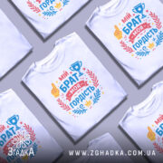 Футболка мій брат моя гордість, біла, зображена на манекені, фон світло-сірий, принт містить текст 'мій брат моя гордість' з жовтою рукою, кубком та декоративними елементами у червоному та блакитному кольорах.