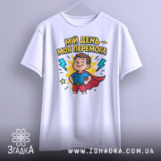 Футболка мій день перемога, біла, підвішена на вішалці, фон світло-сірий, принт з хлопчиком у червоному плащі, оточеним блискавками і написом.