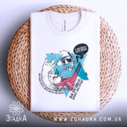 Футболка мій лук: біла футболка, зображена зверху на плетеному фоні, принт з бородатим чоловіком у капелюсі, яскраві кольори принта, фон натуральний.