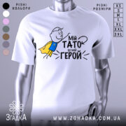 Футболка мій тато герой, біла, зображена з фронтального ракурсу, на фоні світло-сірого кольору, принт з малюнком хлопчика в жовтому плащі та текстом "Мій тато це мій герой".