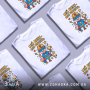 Футболка мій внук білого кольору, зображена з фронтального ракурсу на манекені, фон світло-сірий, принт з веселим супергероєм у синій футболці з червоним плащем, тримає кубок та медалі, оточений зірками.