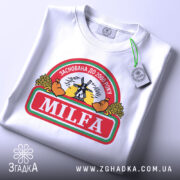 Футболка мілфа заснована білого кольору, зображена в складеному вигляді, фон світлий, принт на футболці включає текст 'MILFA' та малюнок вітряка, прикріплена бірка з зеленим шнурком.