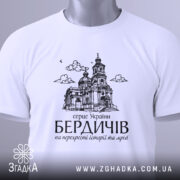 Футболка місто Бердичів подарунок, біла, складена на поверхні, фон світло-сірий, принт з архітектурним зображенням церкви, з зеленим ярликом.