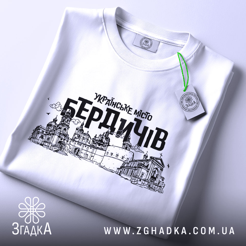 Футболка місто Бердичів, біла, зображена зверху, складена на поверхні, фон світлий, принт містить чорний контурний малюнок архітектурних пам'яток Бердичева з написом 'УКРАЇНСЬКЕ МІСТО БЕРДИЧІВ', на футболці є етикетка з зеленим шнурком.