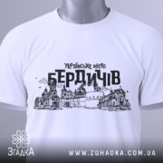 Футболка місто Бердичів, біла, зображена зверху, складена на поверхні, фон світлий, принт містить чорний контурний малюнок архітектурних пам'яток Бердичева з написом 'УКРАЇНСЬКЕ МІСТО БЕРДИЧІВ', на футболці є етикетка з зеленим шнурком.