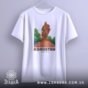 Футболка місто Коростень, біла, підвішена на вішалці, фон світло-сірий, принт з зображенням воїна на кам'яній основі з зеленим фоном.