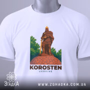 Футболка місто Коростень, біла, складена на столі, фон світло-сірий, принт з зображенням воїна на кам'яній основі, етикетка з зеленим шнурком.