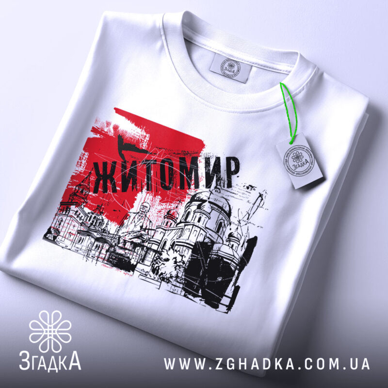 Футболка місто Житомир, біла, складена на поверхні, фон світло-сірий, принт червоного кольору з написом 'Житомир' та малюнком будівель.