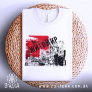 Футболка місто Житомир, біла, складена на плетеній основі, фон світло-сірий, принт червоного кольору з написом 'Житомир' та графічними елементами.