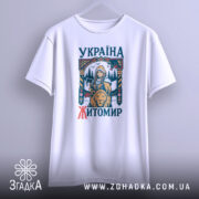 Футболка місто Житомир, біла, підвішена на вішалці, фон світло-сірий, принт з дівчиною, сокирою та левом, текст 'УКРАЇНА ЖИТОМІР' у кольорах синього та червоного.