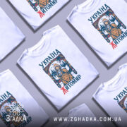 Футболка місто Житомир, біла, зображена на манекені, фон світло-сірий, принт містить зображення дівчини з сокирою та лева, текст 'УКРАЇНА ЖИТОМІР' виконаний у кольорах синього та червоного.