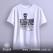 Футболка місто Звягель, білого кольору, підвішена на вішалці, фон нейтральний, принт з зображенням замку та текстом, виглядає стильно.