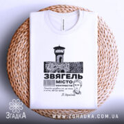 Футболка місто Звягель, білого кольору, складена на плетеній основі, фон світлий, принт містить зображення замку та текст, виглядає акуратно.