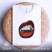 Футболка модна провокація, біла, складена на плетеному кошику, фон світло-сірий, принт з червоними губами та золотими зубами, деталі з діамантом на одному з зубів.