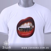 Футболка модна провокація, біла, складена на столі, фон світло-сірий, принт з червоними губами та золотими зубами, на футболці є етикетка з зеленим шнурком.