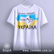 Футболка моя хата всюди, біла футболка з коротким рукавом, підвішена на вішалці, фон світлий, принт з картою України, жовто-блакитні кольори, напис '603.548км²' та малюнок голуба.