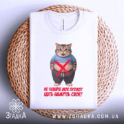 Футболка моє пузіко, біла, зображена зверху на плетеному кошику, фон світло-сірий, принт з котом у синій футболці, текст червоного кольору, видно етикетку на комірці.