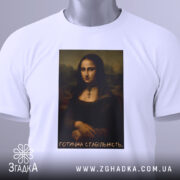 Футболка Мона Ліза білого кольору, лежить на поверхні, з видимим етикеткою, фон світло-сірий, принт з портретом Мона Лізи з написом 'Готична стабільність'.