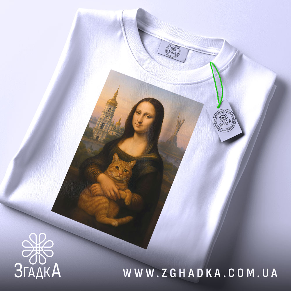 Футболка Мона Ліза Київ, біла, складена на столі, фон світло-сірий, принт зображає Мону Лізу з котом, на футболці є етикетка з зеленим шнурком.