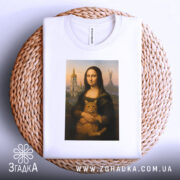 Футболка Мона Ліза Київ, біла, складена на плетеній основі, фон світло-сірий, принт зображає Мону Лізу з котом, футболка виглядає акуратно та стильно.