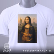 Футболка Мона Ліза Київ, біла, складена на столі, фон світло-сірий, принт зображає Мону Лізу з котом, на футболці є етикетка з зеленим шнурком.